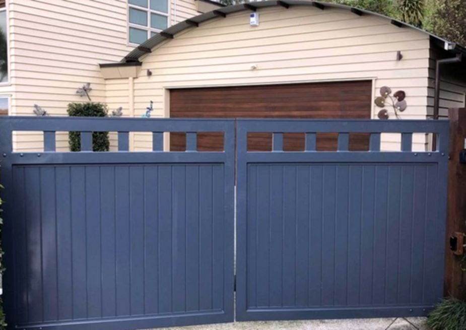 Slate blue solid vertical-board double swing gate with a spindle top rail, closed in front of a two-story house