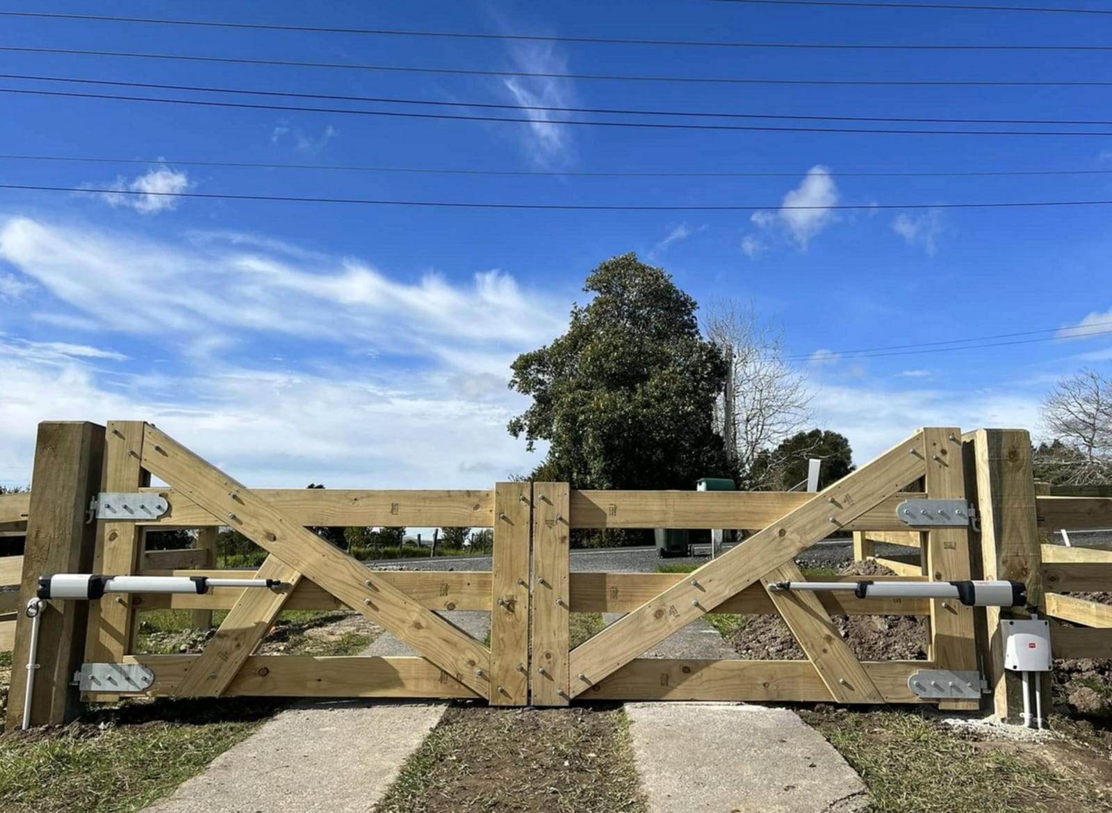 New treated-timber ranch-style double gate with diagonal bracing, fitted with two linear arm gate operators on fresh concrete footings