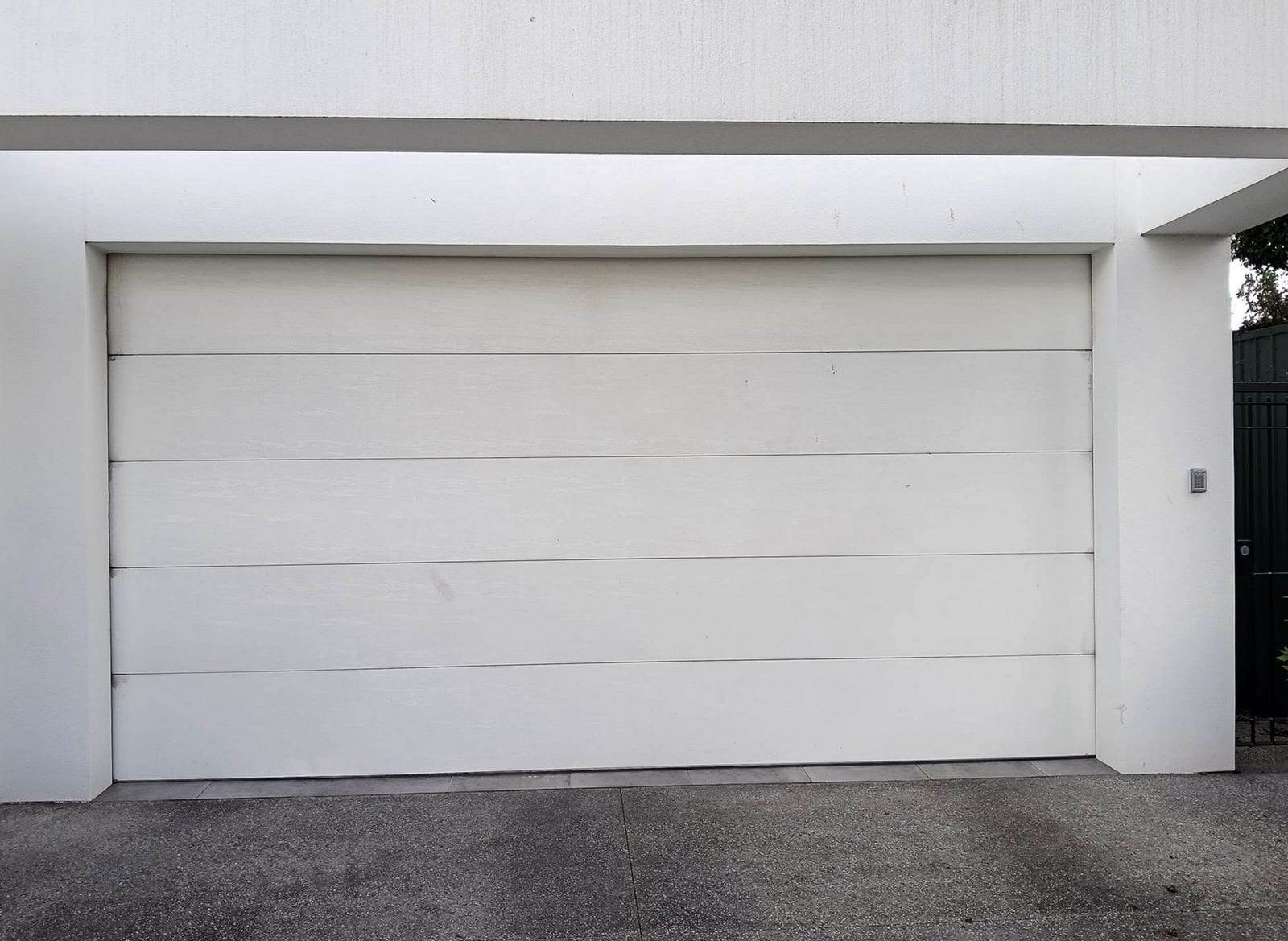 White double-wide flush-panel sectional garage door on a modern white house, with a keypad mounted on the wall beside it