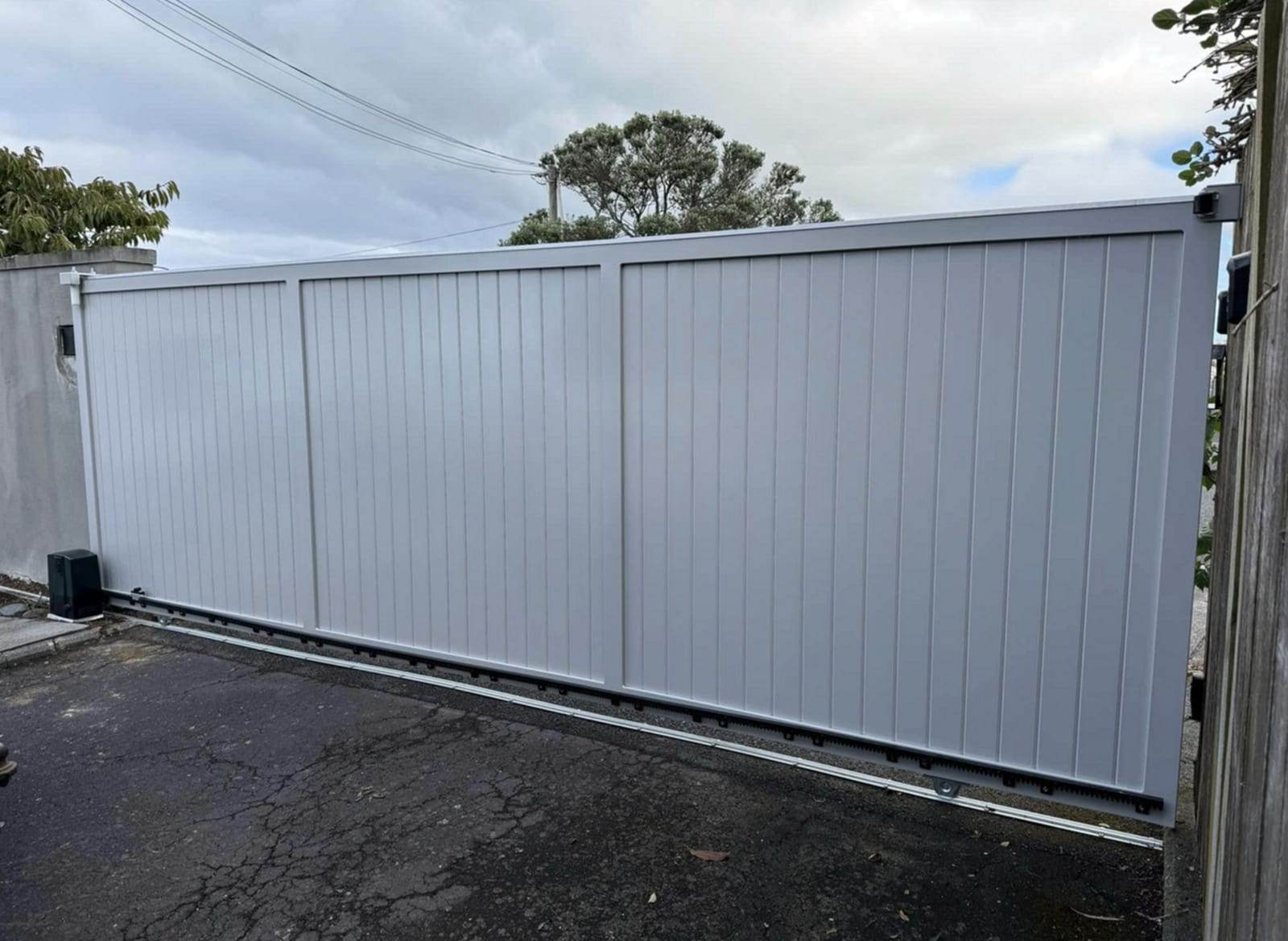 Light gray solid-panel privacy sliding gate riding on a ground track, with the slide gate operator mounted at the left post