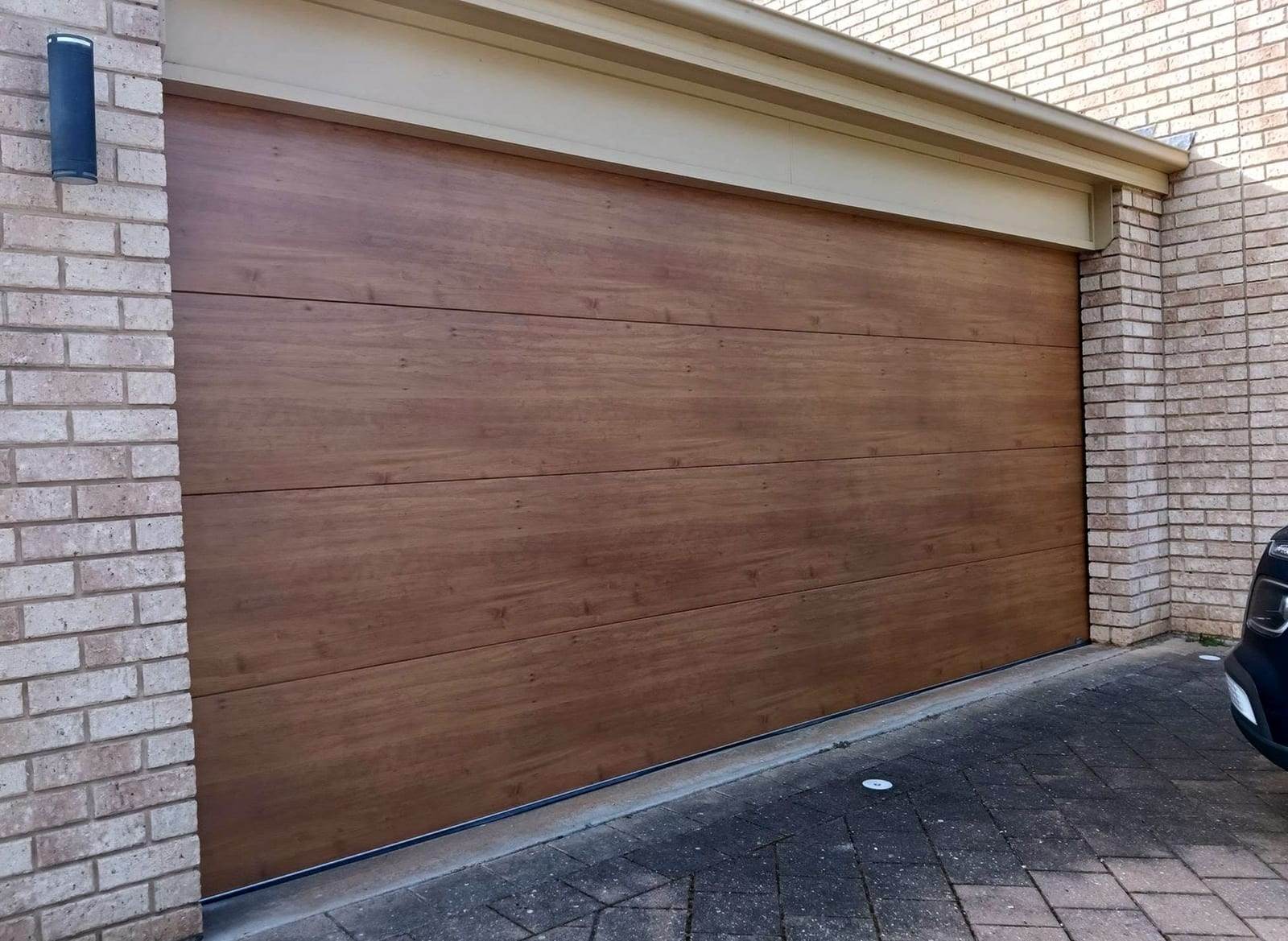Double sectional garage door with a warm walnut woodgrain finish and long flush panels, in a tan brick garage