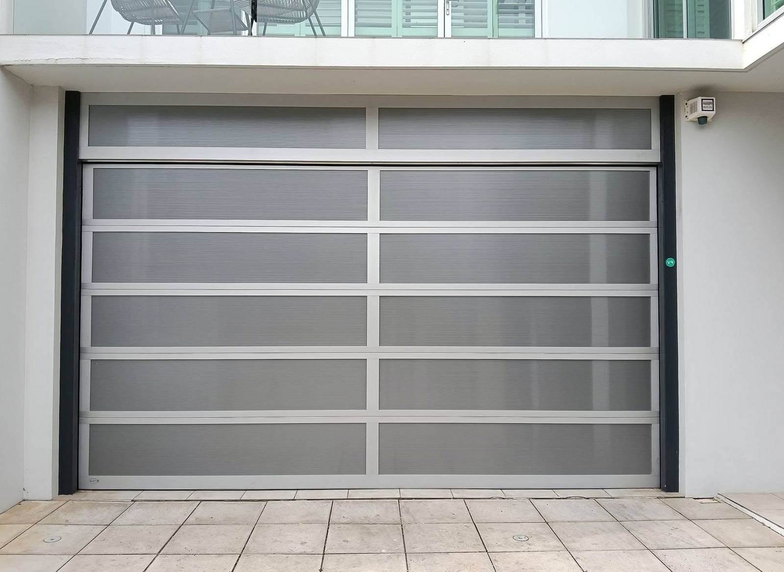 Full-view garage door with a silver aluminum frame and frosted panels, under the balcony of a modern white house