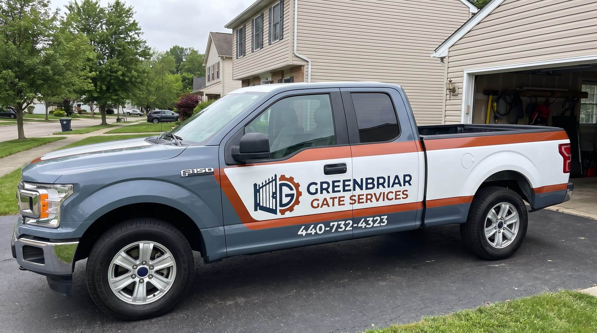 Greenbriar Gate Services pickup truck, wrapped in slate gray with an orange stripe and the company logo and phone number, parked in a residential driveway in Parma